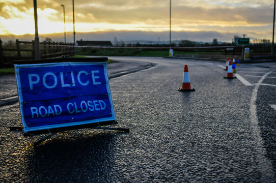 Police road closed sign and traffic cones seal off a road following an incident