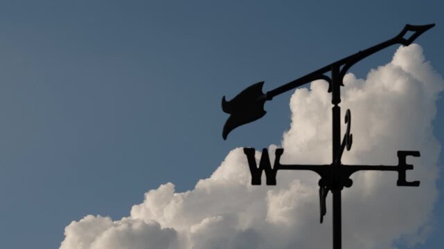 Time-lapse storm cloud building and drifting across blue sky behind a classic weather vane silhouette, illustrating shifting weather, changing direction, and the passage of time