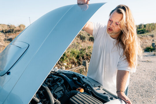 Man Inspecting Car Engine Outdoors During a Sunny Day