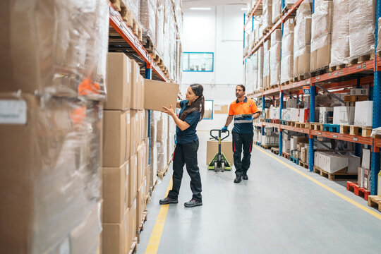 Warehouse workers organizing packages on shelve, using pallet jack