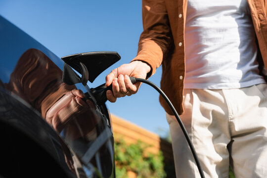The man connects the charger to the electric car