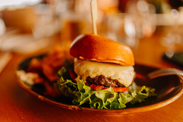 Gourmet cheeseburger with melted cheese, fresh lettuce, and tomato served on a wooden plate alongside crispy fries in a restaurant setting
