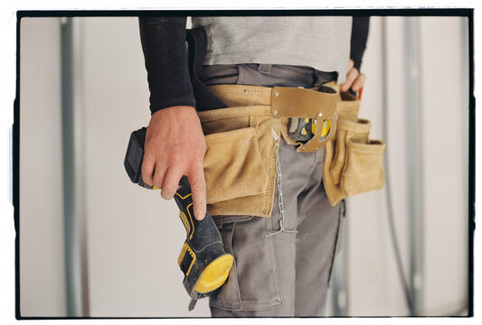 Anonymous worker with power tools and belt standing at construction