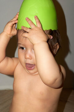 A little girl having fun pretending a green bowl is her hat.