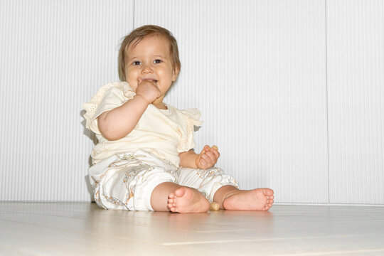 Cute Baby Sitting on Floor and Smiling With Hands in Mouth