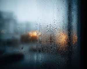 Obraz premium Raindrops window glass create moody atmosphere with blurred city lights glowing warmly through cold wet surface, evoking energy despite poverty
