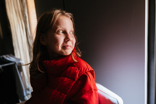 Child in Bright Red Jacket Gazes Thoughtfully by Window