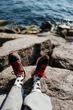 Legs in Sneakers Resting on Rocks by Water