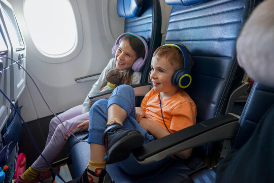 Two kids laugh while watching in-flight movie on airplane