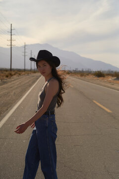 Model Poses on an Empty Road With Mountains in the Background