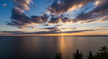Fototapeta premium Sunset over a calm body of water, with dramatic clouds and a treeline on the horizon