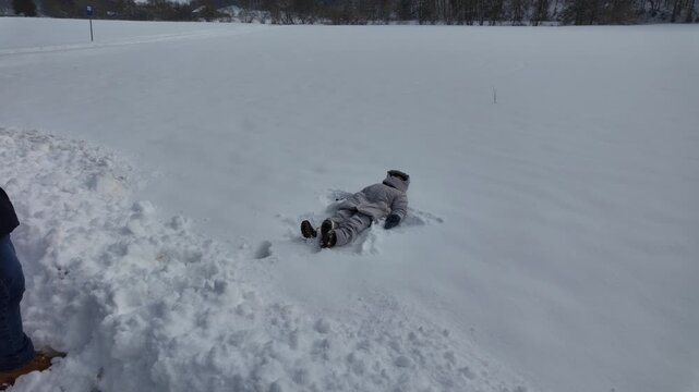 Father throws five year old son into soft snow on open field. Boy making snow angel, winter family fun and childhood joy outdoors.