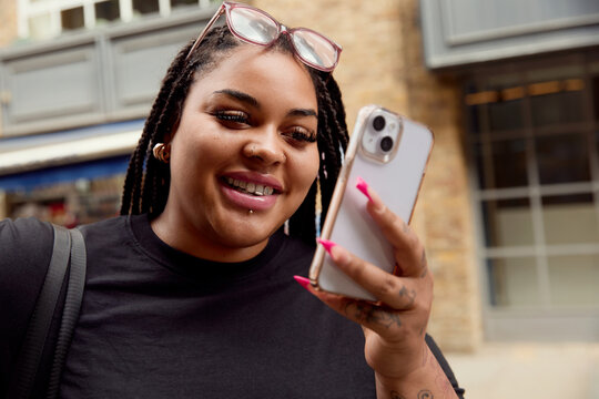 Woman Smiling While Looking at Phone on London Street