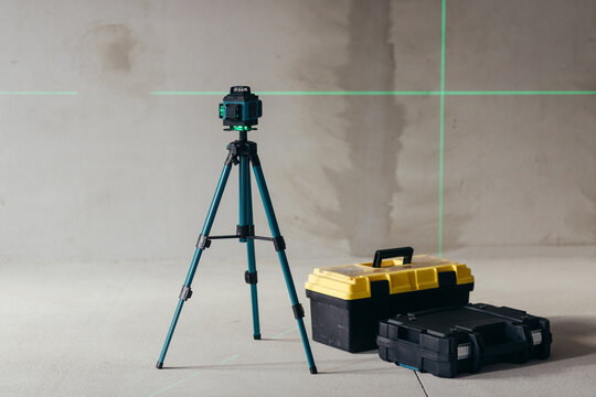 Laser Level On Tripod Projecting Green Cross Lines Beside Tool Cases. Construction Site Measurement Setup.
