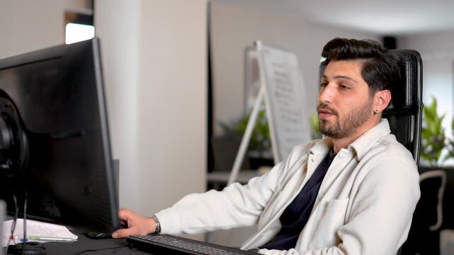 In a modern office setting, the young man stares blankly at the computer screen.