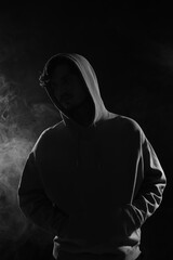 Man in hood on dark background with smoke. Black and white effect