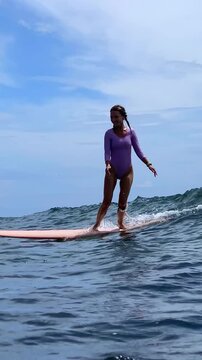 Woman Surfer Standing On Longboard Graceful Glide Along Glassy Ocean Purple Swimsuit Calm Stance Distant