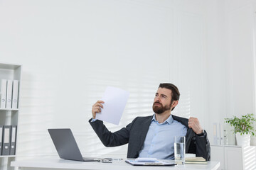 Fototapeta premium Man suffering from heat at table near white wall indoors, space for text