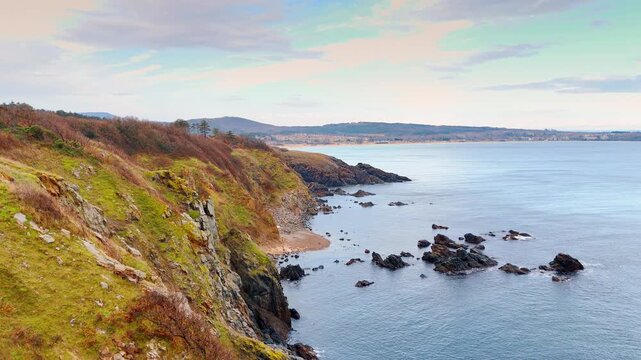 Elevated view of a rocky bay and sandy beach. High angle shot of a coastline featuring rocky outcrops, a small sandy patch, and a distant coastline.