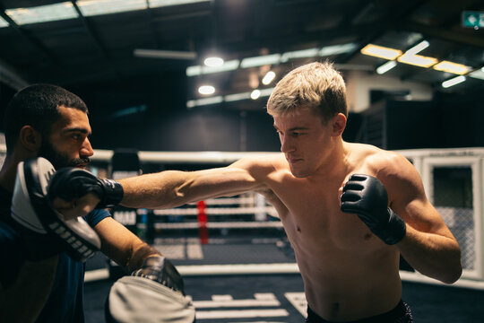 Martial artist practicing combos with coach in MMA gym