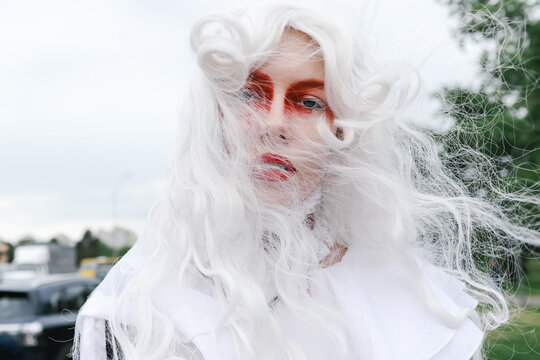 A woman in a wig and a bright costume walks through the city