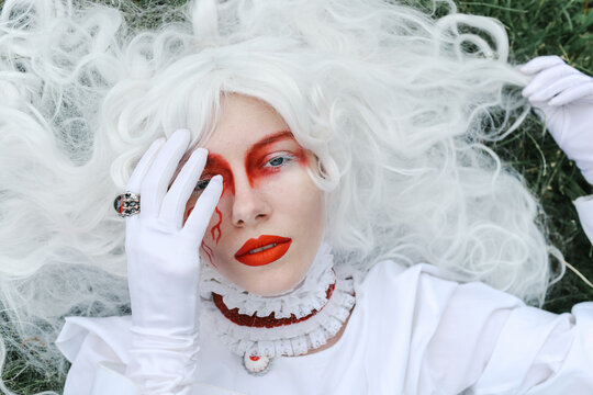A woman in a wig and a  bright costume walks in the park