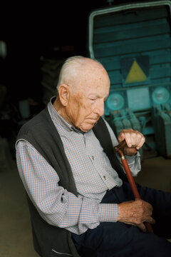 Elderly man in deep thought while sitting with cane in workshop