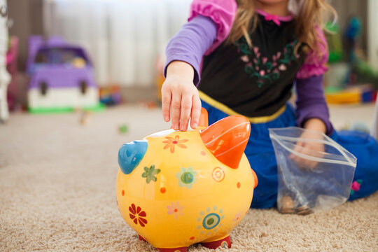 Toddler in princess dress puts money in her piggy bank. 