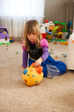 Toddler in princess dress puts money in her piggy bank. 