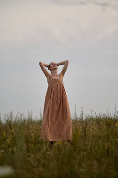 Woman standing freely through a field at dusk