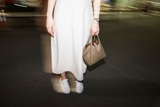 Woman in white dress with handbag walking on city street at nigh