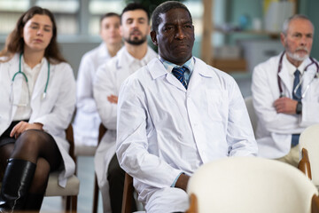 Fototapeta premium Adult male doctor listening to lecture and watching presentation with colleagues in lecture hall