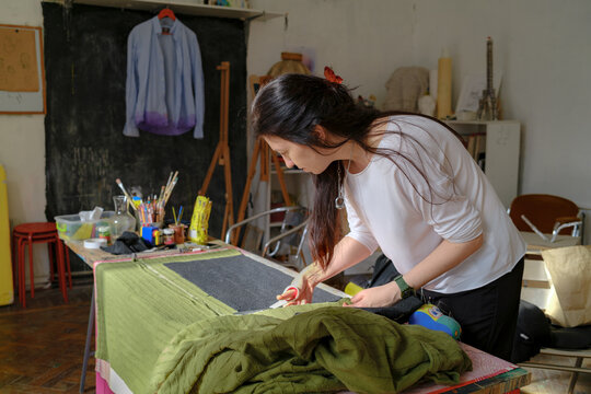 The woman is cutting fabric on the table 
