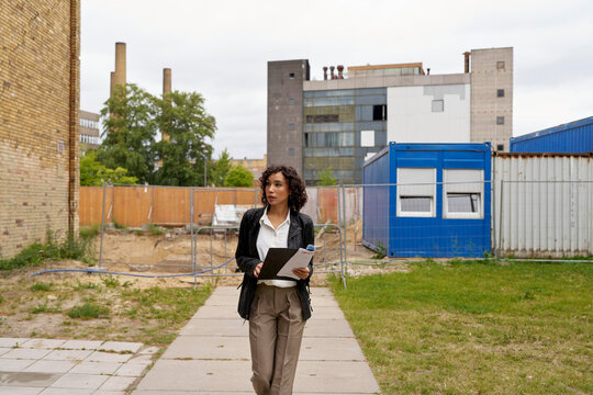 Woman Walks Through Construction Site in Urban Area With Clipboard