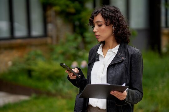 Woman engaged with phone while holding documents outdoors