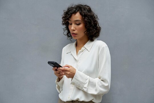 Woman using smartphone while standing against gray wall indoors