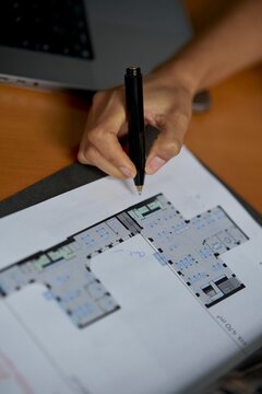 Hand Examining Architectural Plans on Wooden Desk Space