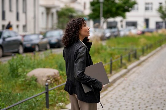 Woman Walking in Urban Area While Holding a Notebook