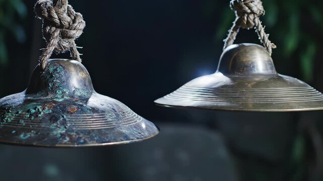 Two Ancient Metal Cymbals Hanging by Ropes with Weathered Patina in Outdoor Garden Setting