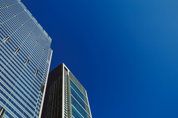 Obraz premium Tall buildings reach towards the blue sky in a busy city during a clear day in midday hours with no clouds present