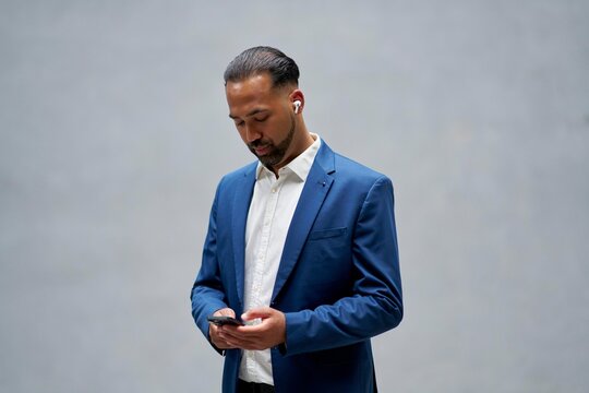 Man Using Smartphone While Wearing Wireless Earbuds in Indoor Setting