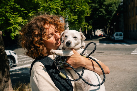 Woman Holds White Dog in City During Sunny Day