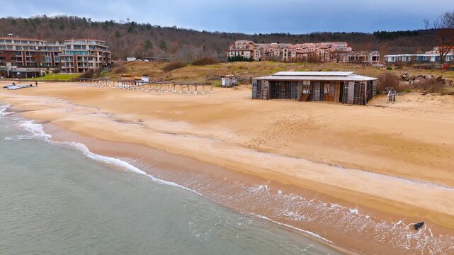 Empty sandy beach with wooden structures and resort buildings. Wide view of a coastal area with temporary beach shacks and distant hotels.