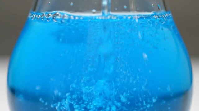 Refreshing blue liquid with energetic bubbles and fizzing action in a clear glass, creating a vibrant and cool sensation.
