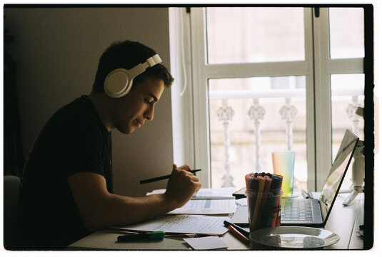 Young Man Studying at a Desk With Headphones in Bright Room