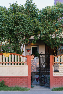 An adult woman stands at a garden gate in a quiet neighborhood