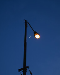 Street lamp glowing at dusk with crescent moon in blue evening sky