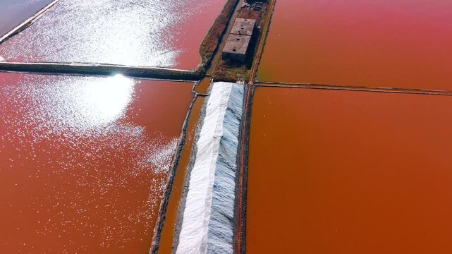 Salt storage pile between colorful evaporation ponds. Aerial top down perspective of a white salt ridge separating sunlit pink and brown saline pools.