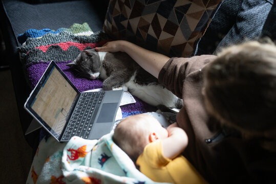 A cat sleeps next to a mother and baby on the couch while she works