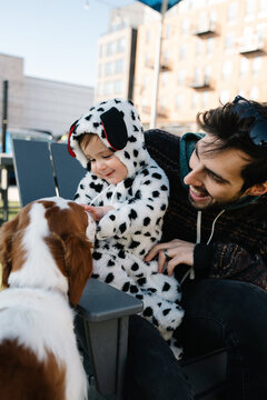 A little boy in a puppy costume and his father pet a dog